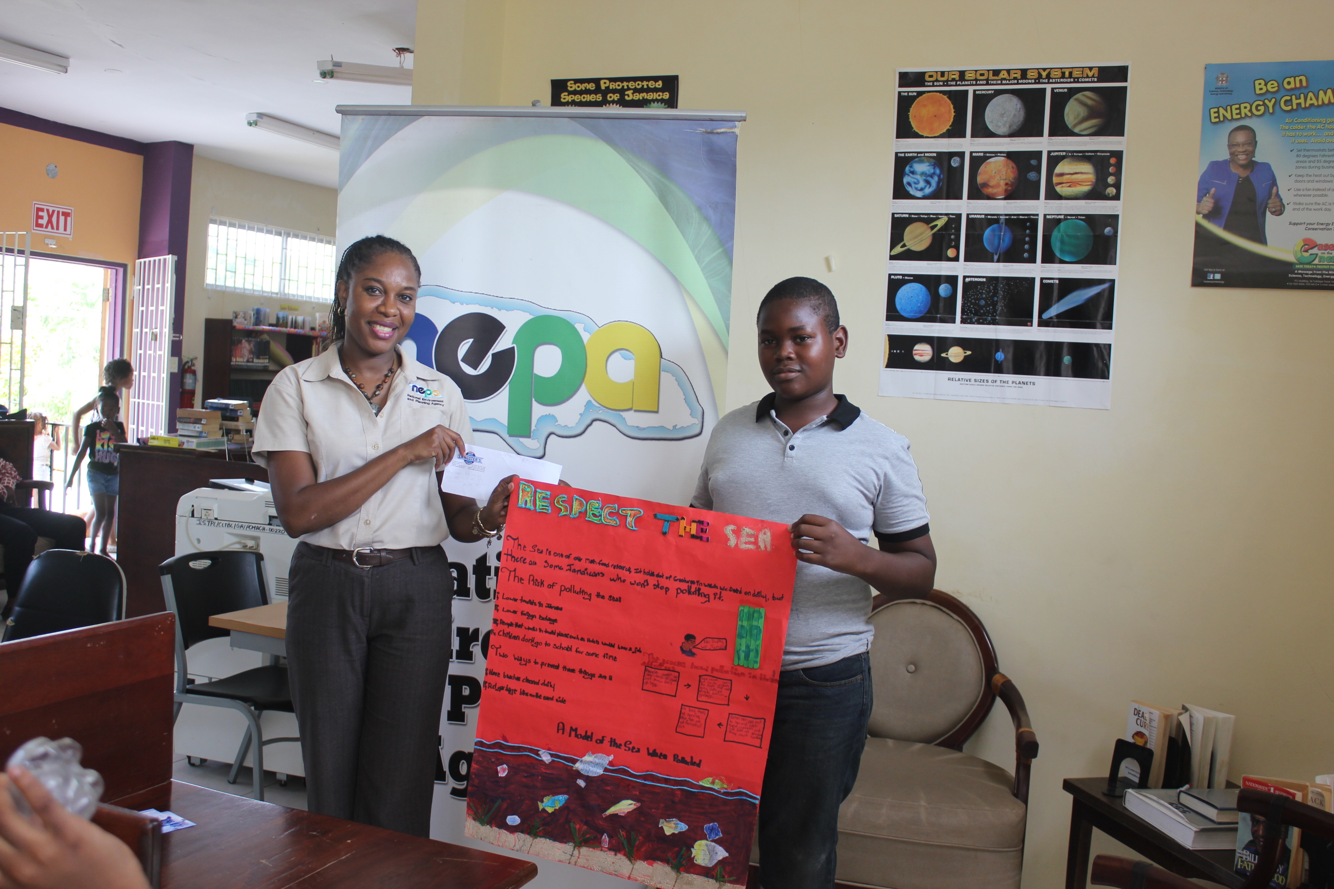 Kay-Ann Miller (l), Senior Librarian, NEPA, with Andre Bailey (r) of the Clarks Town Branch Library and winner of Poster Competition during the Annual Sharon O’Connor Documentation Centre Summer Library Programme. Photo credit: NEPA